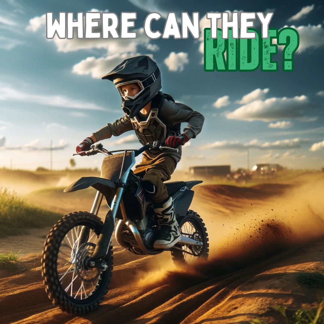 A young rider in full safety gear, including a helmet, gloves, and protective clothing, is riding a dirt bike on a designated dirt bike track