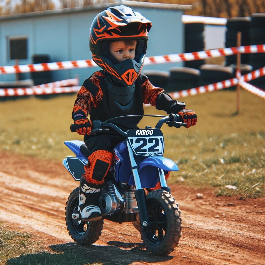 A young child in full motocross gear, including an orange and black helmet, matching jersey, and pants, with protective gloves. The child is riding a small blue RiiRoo motorcycle