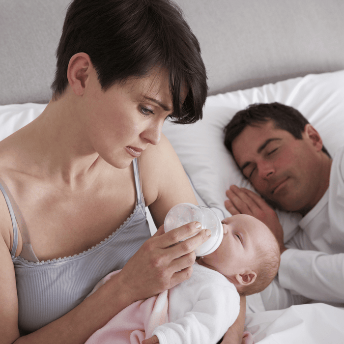 A woman in bed feeding her baby with a bottle