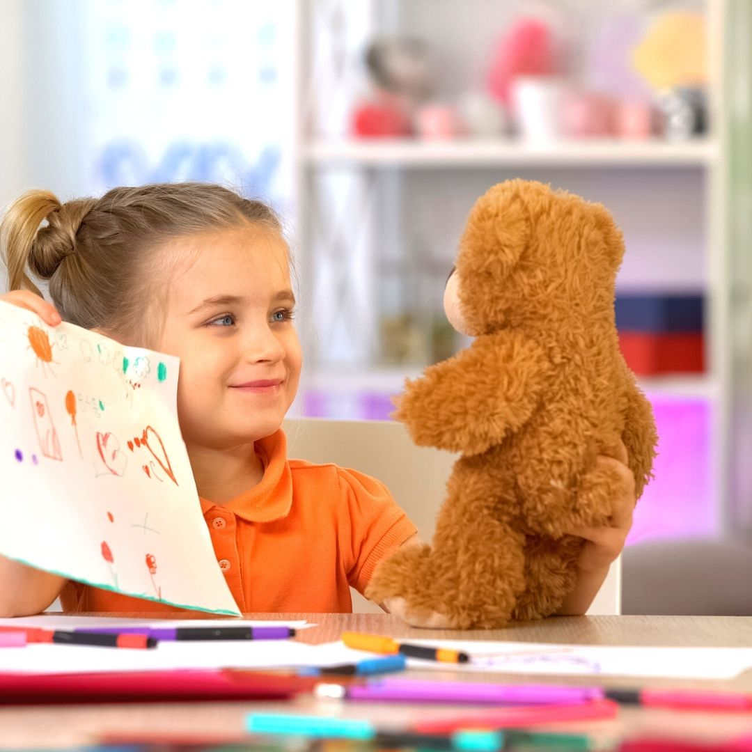 a child showing her teddy bear a picture she has drawn