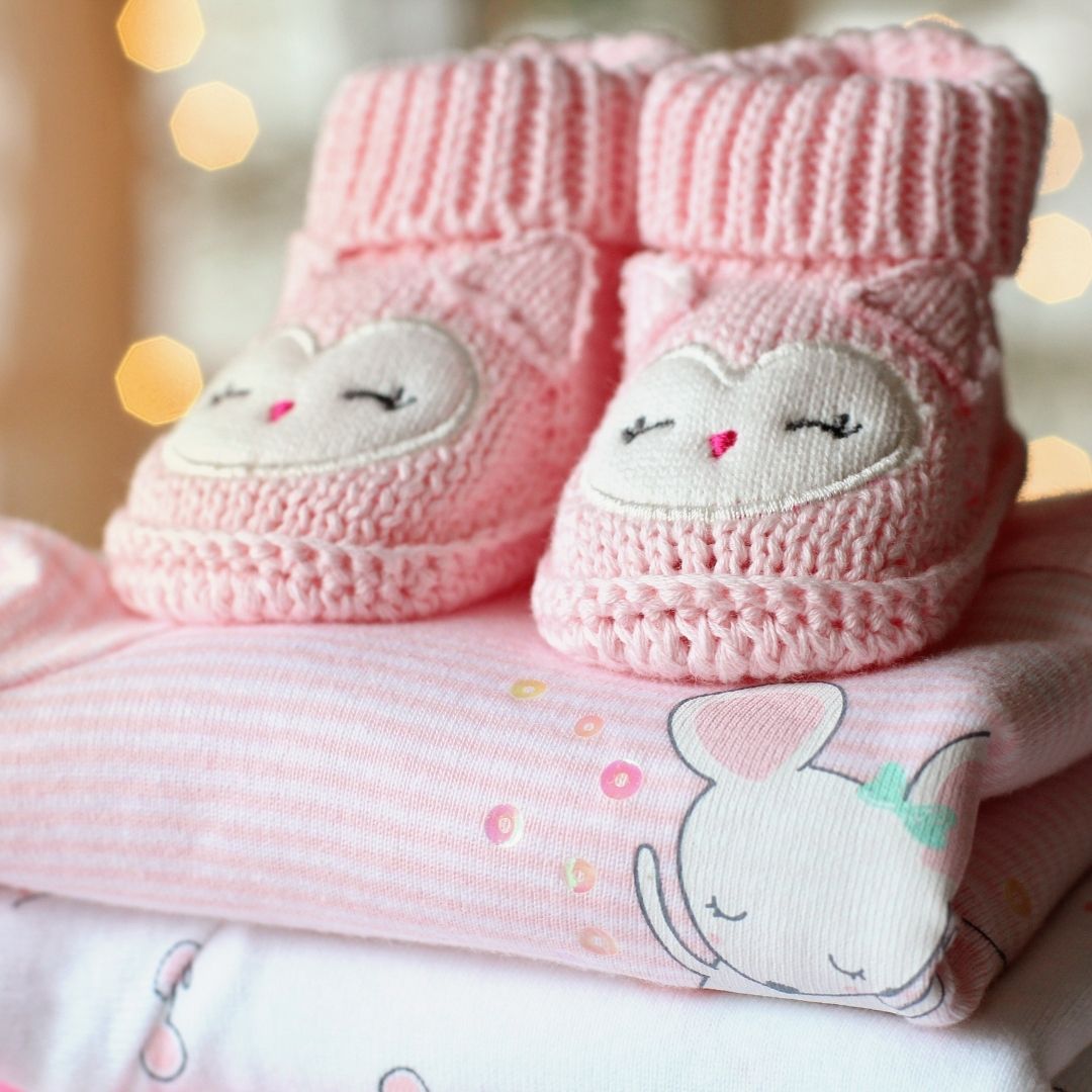 a set of small pink baby booties sitting on some baby clothes