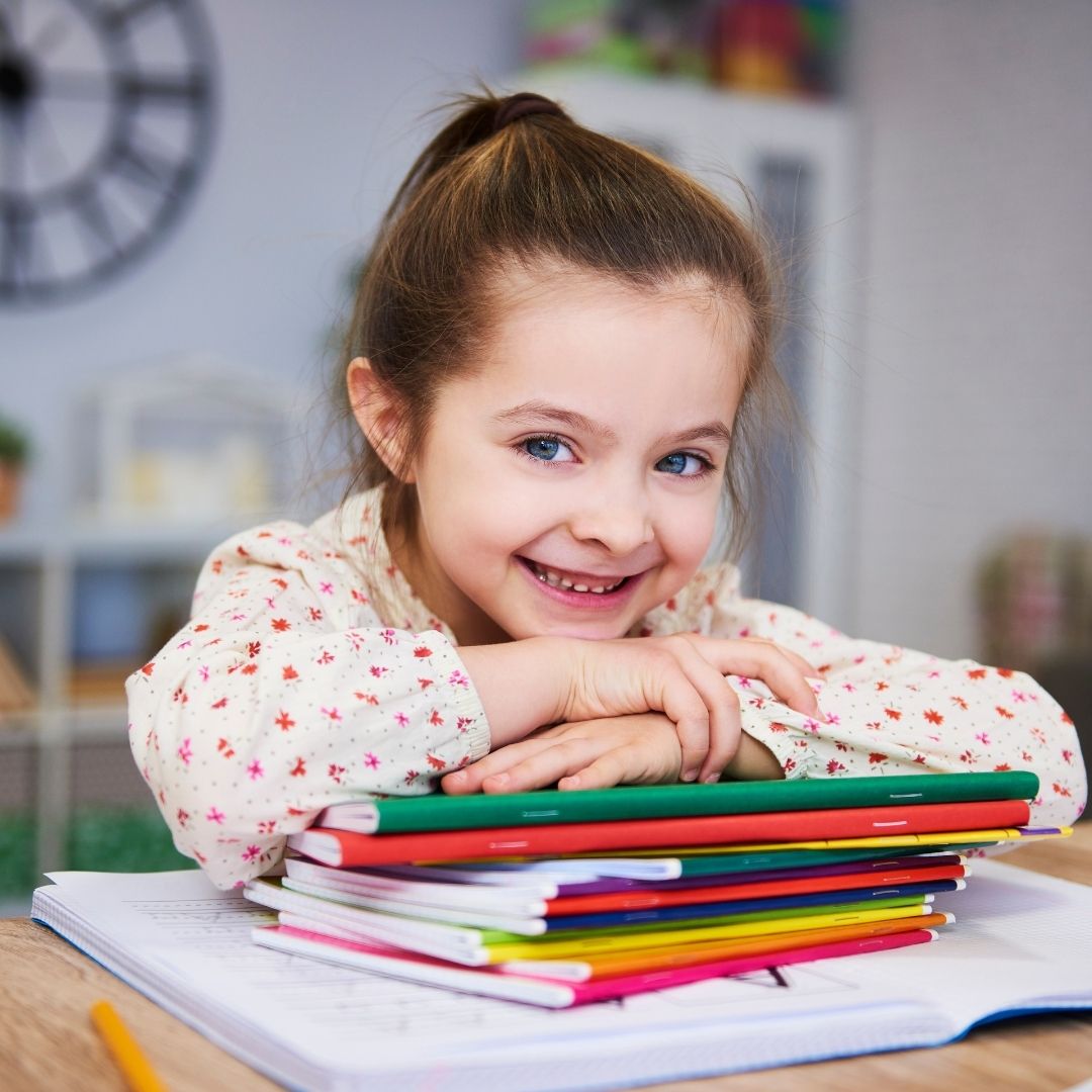child smiling with arms crossed on top of her work books