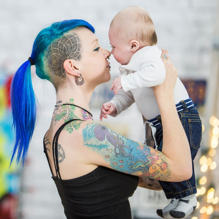 single mother with blue hair holding up her baby