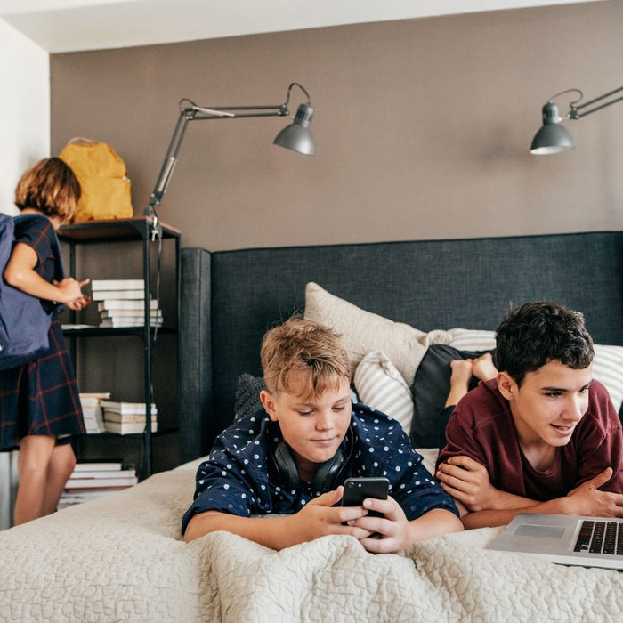 two kids on a bed looking mobile and laptop